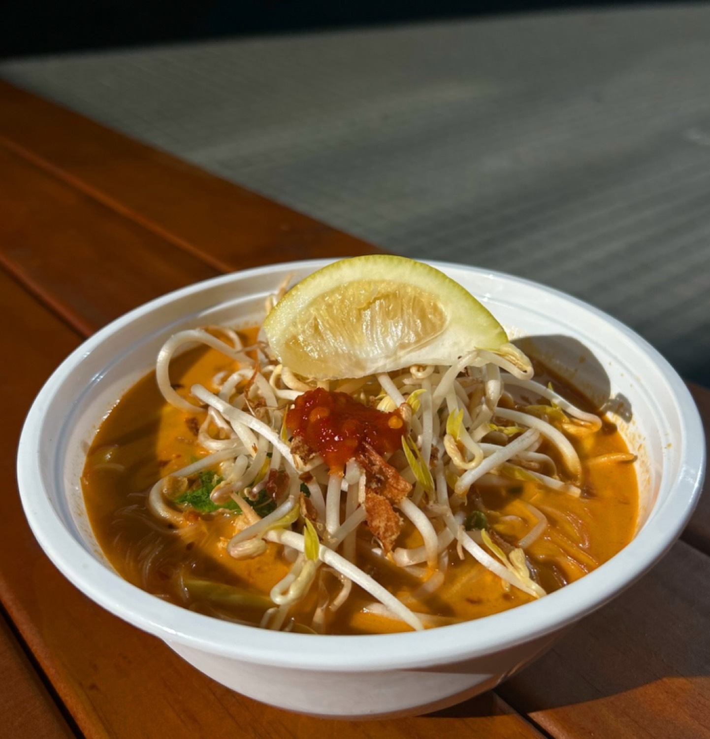 Bowl of laksa with bean sprouts, sambal and a wedge of lime